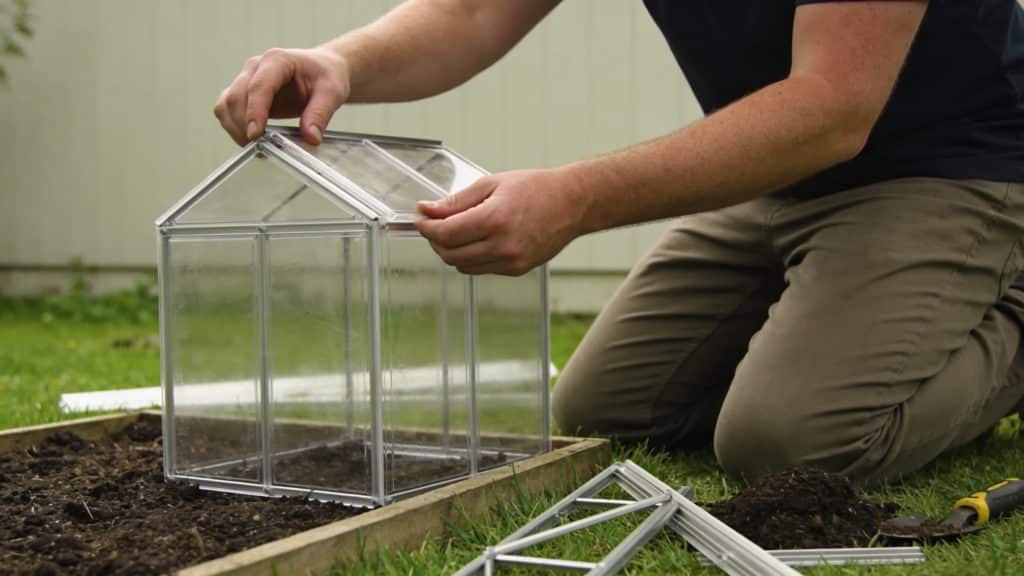 homme agenouille construisant petite serre plastique jardin
