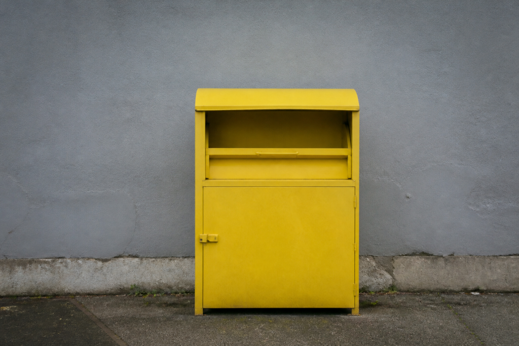 Conteneur jaune pour vetements usages devant un mur gris