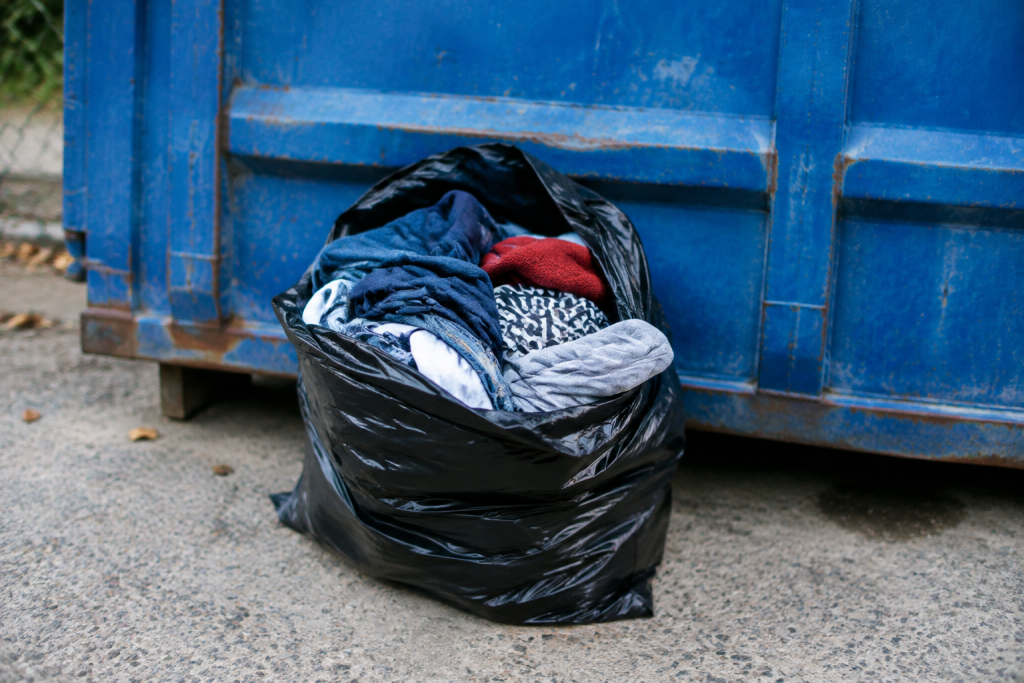 Sac plein de vetements devant un conteneur bleu