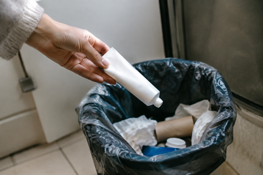 Main jetant tube cosmetique vide dans poubelle